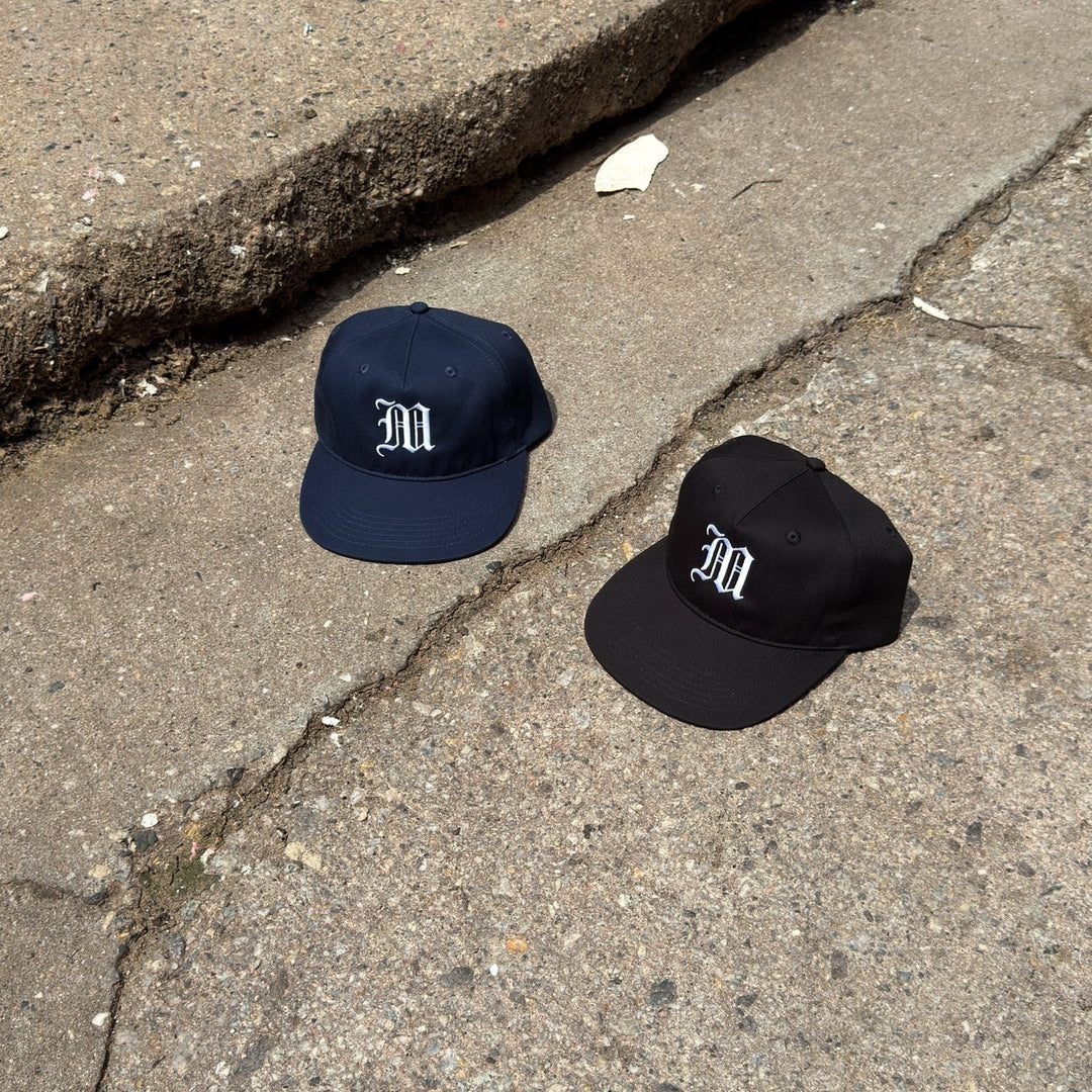 Two caps, one navy and one black, with a logo on a cracked pavement.