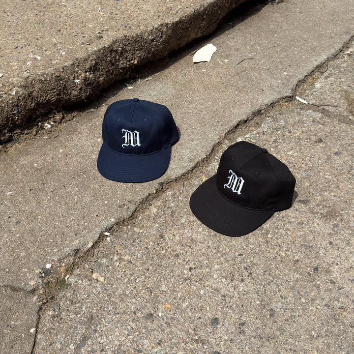 Two caps, one navy and one black, with a logo on a cracked pavement.